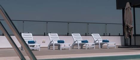 A rooftop pool area with white lounge chairs and a covered umbrella.