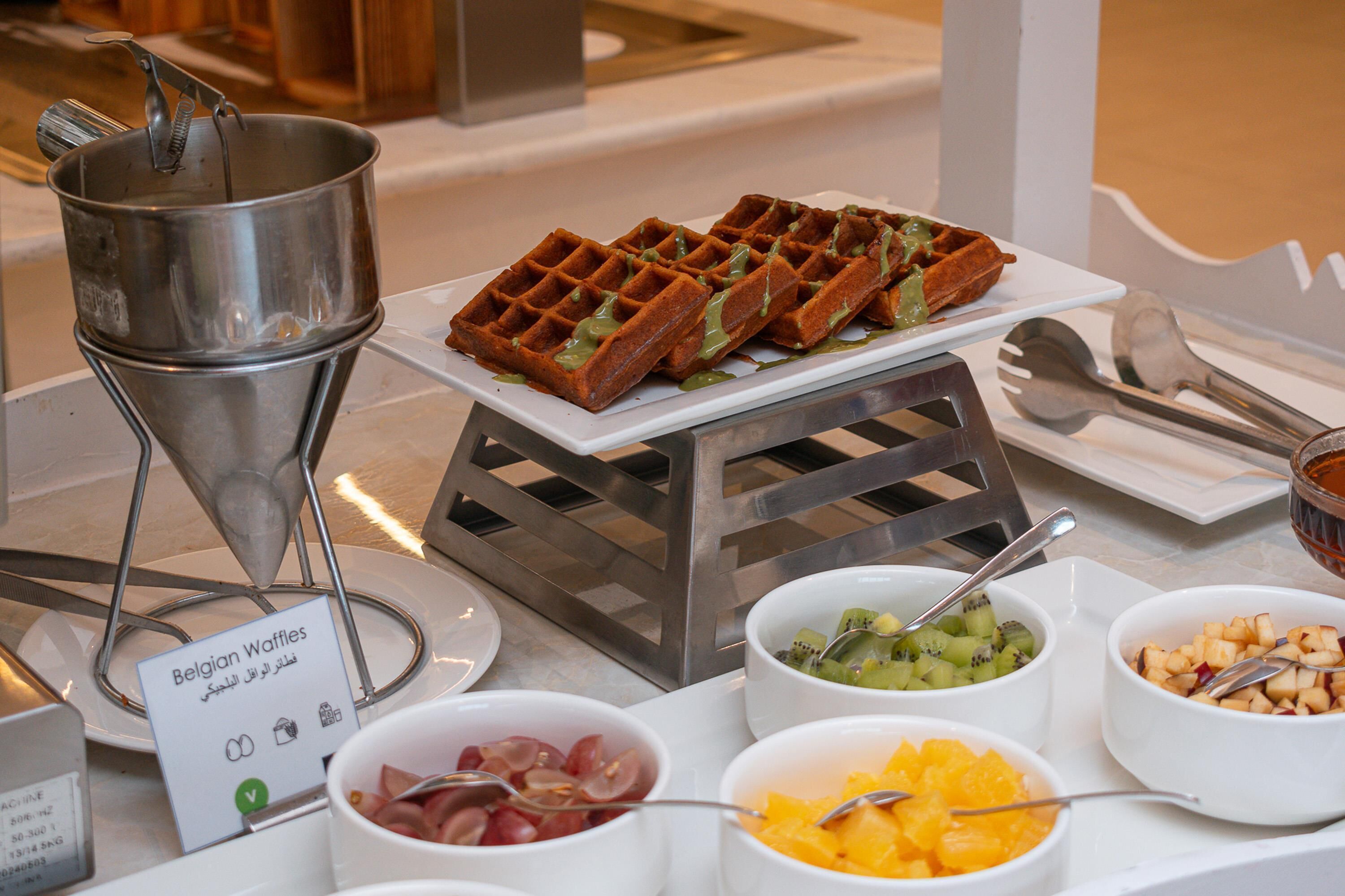 A buffet table with Belgian waffles, fruit bowls, and a waffle iron.