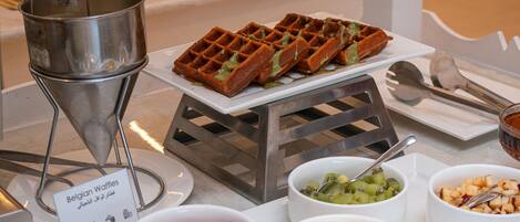 A buffet table with Belgian waffles, fruit bowls, and a waffle iron.