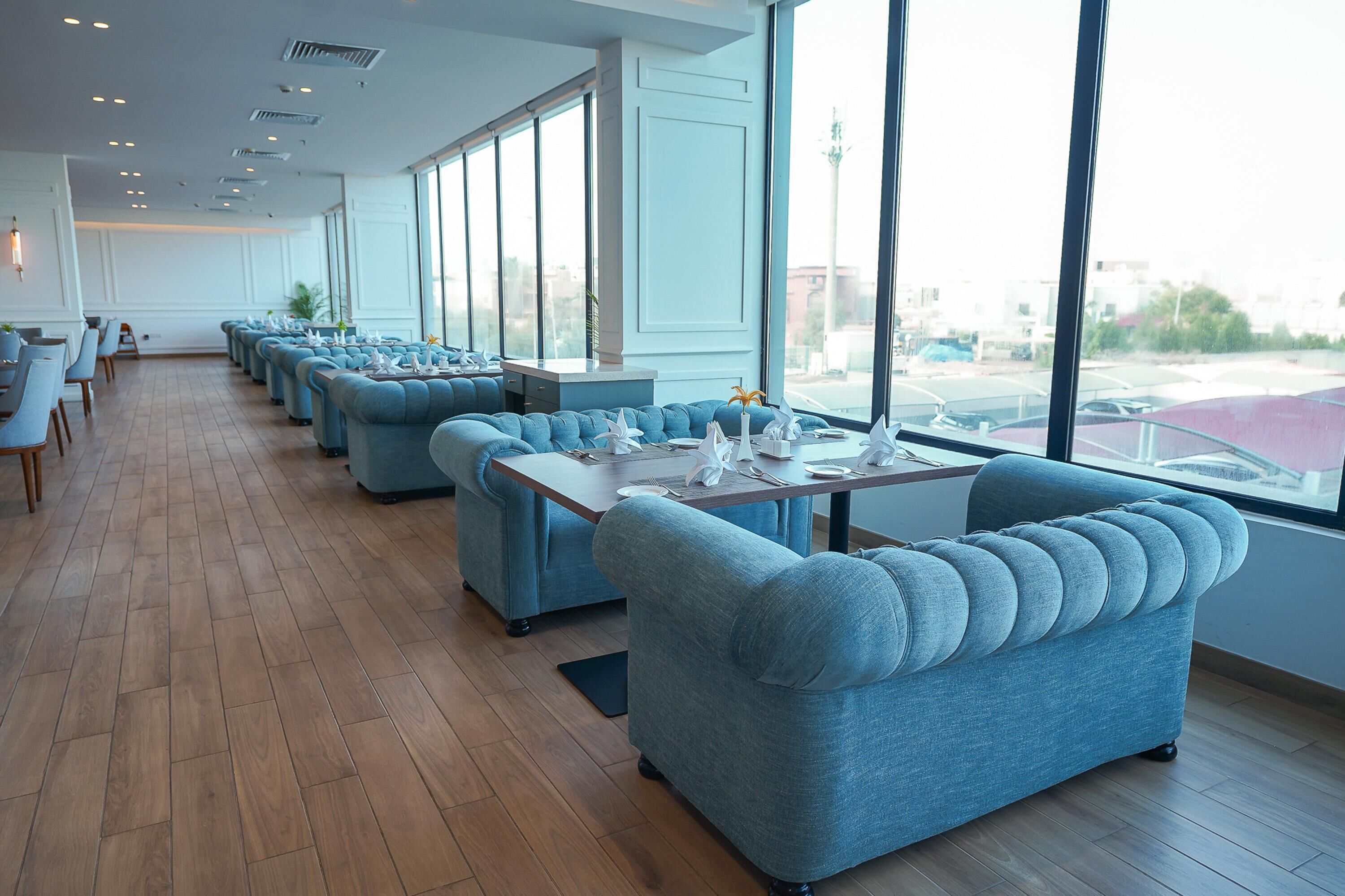 Een modern restaurant met blauwe gestoffeerde banken, houten vloeren en grote ramen met uitzicht op de stad.