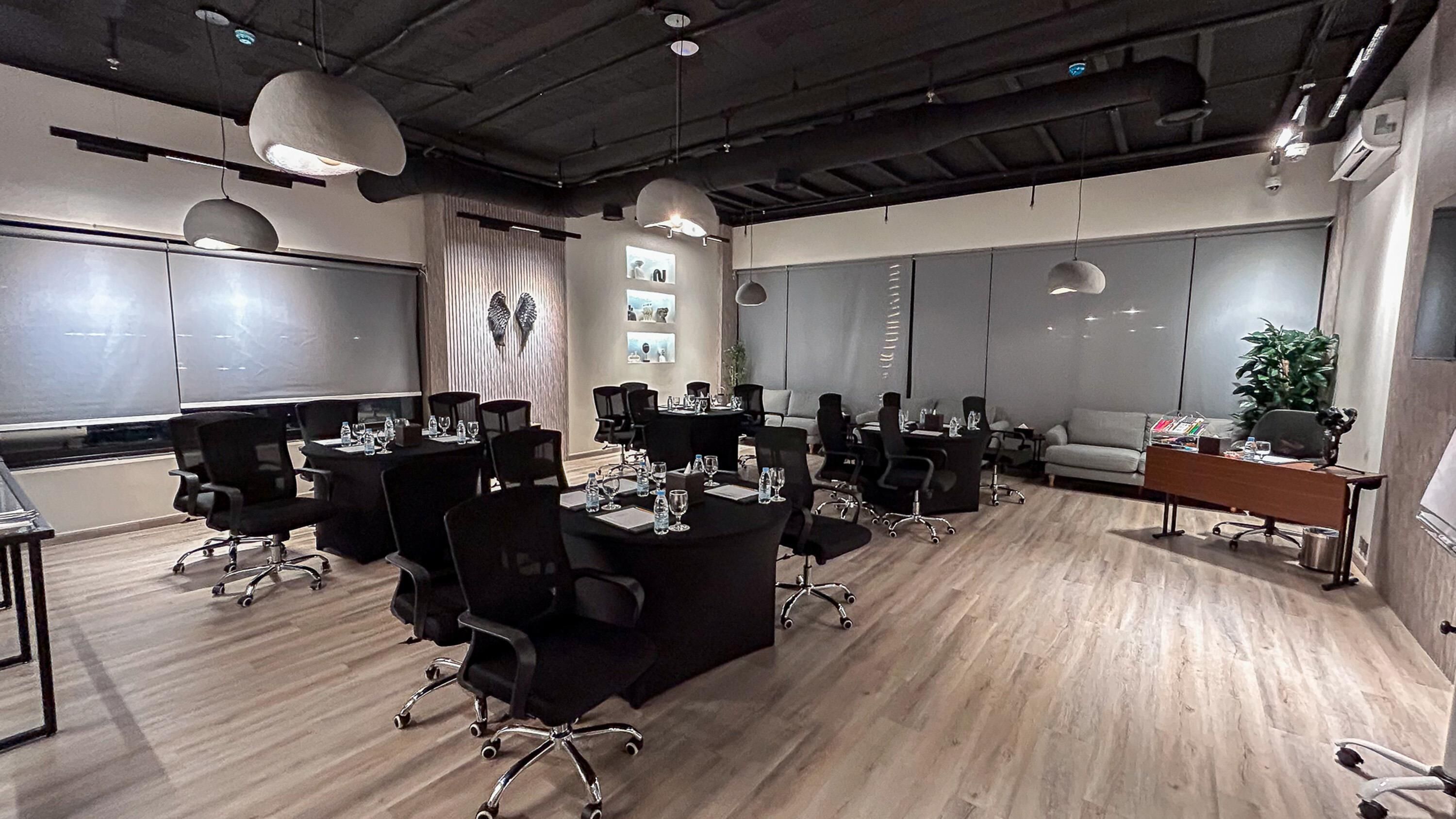 A modern conference room with black chairs, round tables, and a wooden floor.