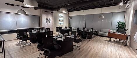 A modern conference room with black chairs, round tables, and a wooden floor.