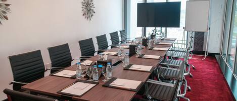 A conference room with a long table, multiple chairs, water bottles, and a large screen.