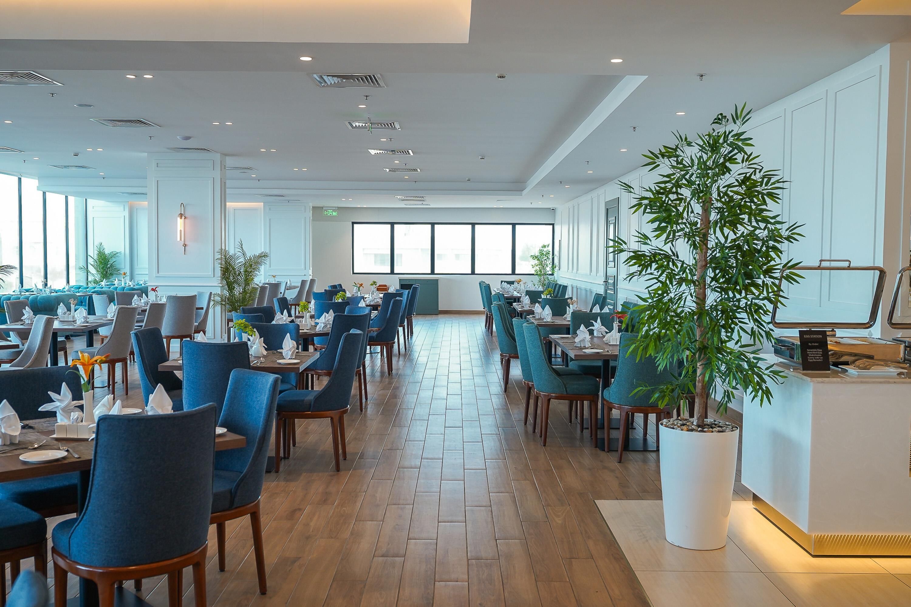 A spacious restaurant with high ceilings, modern lighting, and a central potted plant.