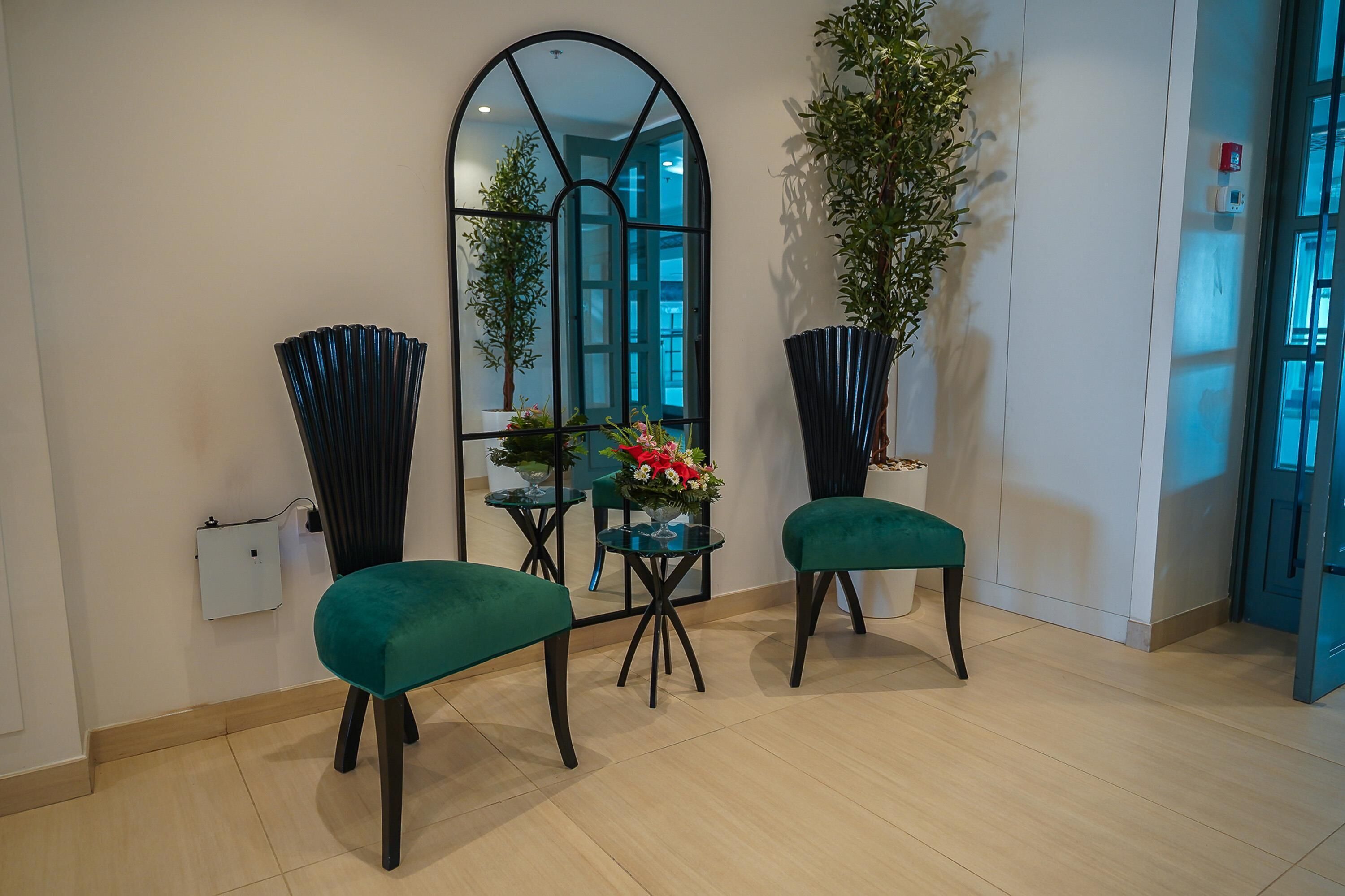 A modern interior with teal upholstered chairs, a glass table, and a large mirror reflecting the room.