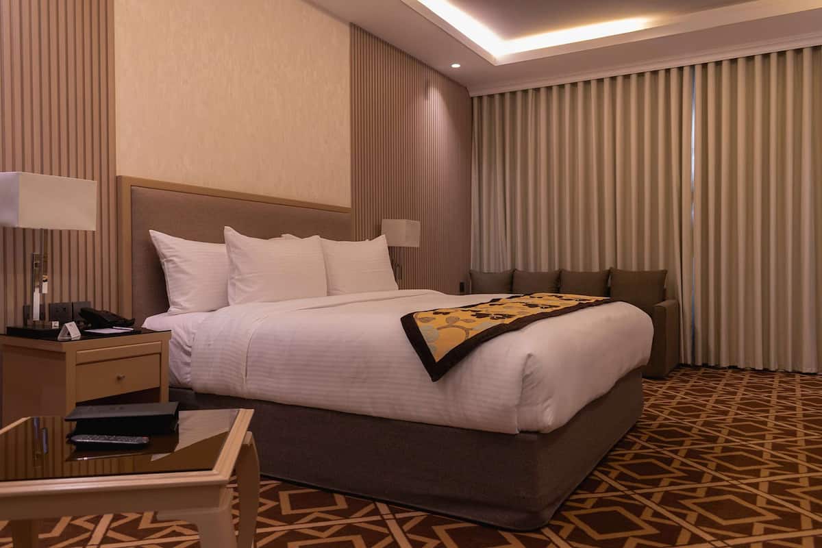 A hotel room with a large bed, bedside tables, a desk, and a patterned carpet.