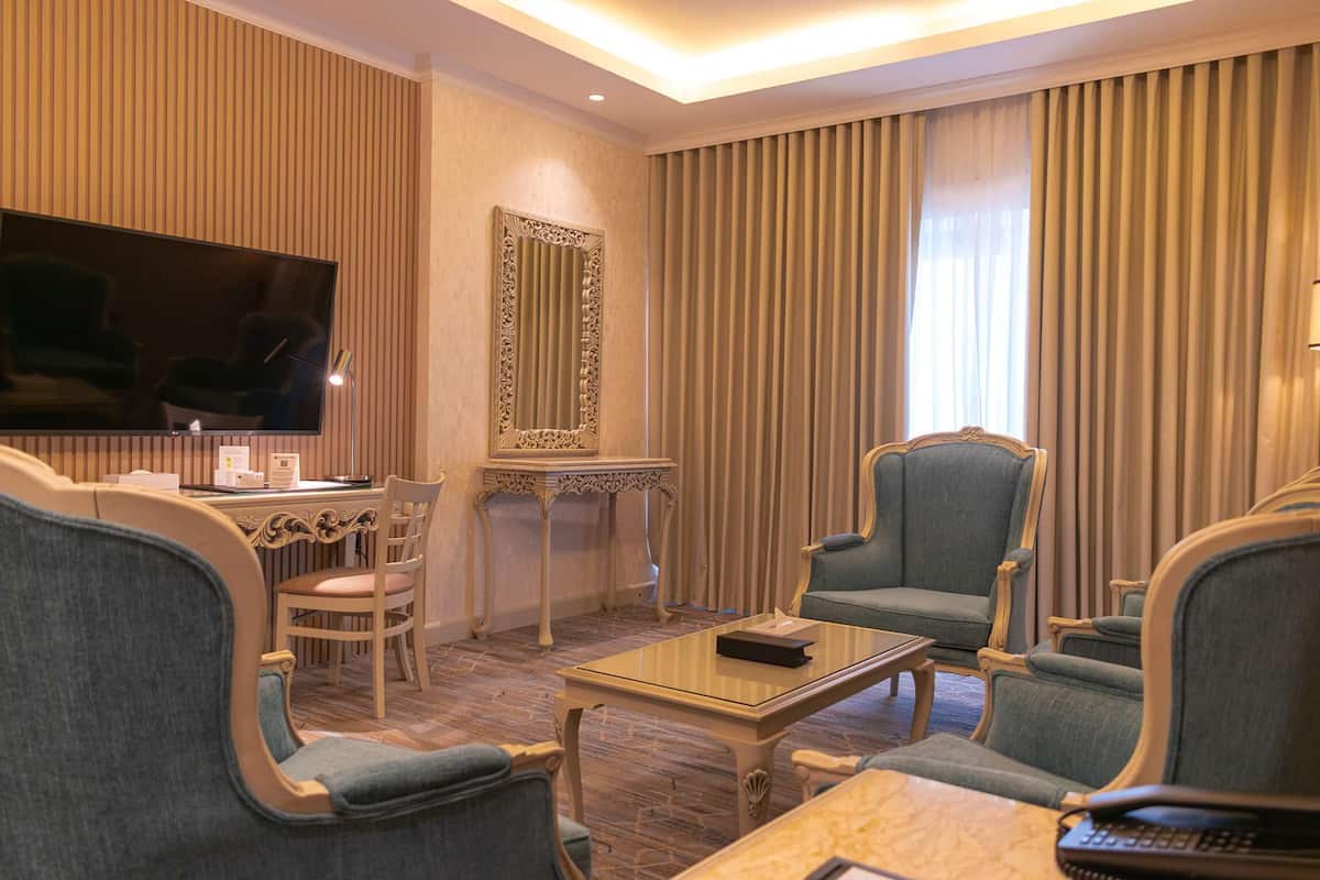 A hotel room with a flat-screen TV, a dining table, chairs, a coffee table, and a large mirror.