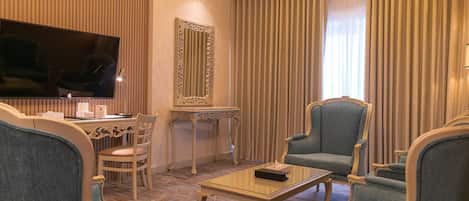A hotel room with a flat-screen TV, a dining table, chairs, a coffee table, and a large mirror.