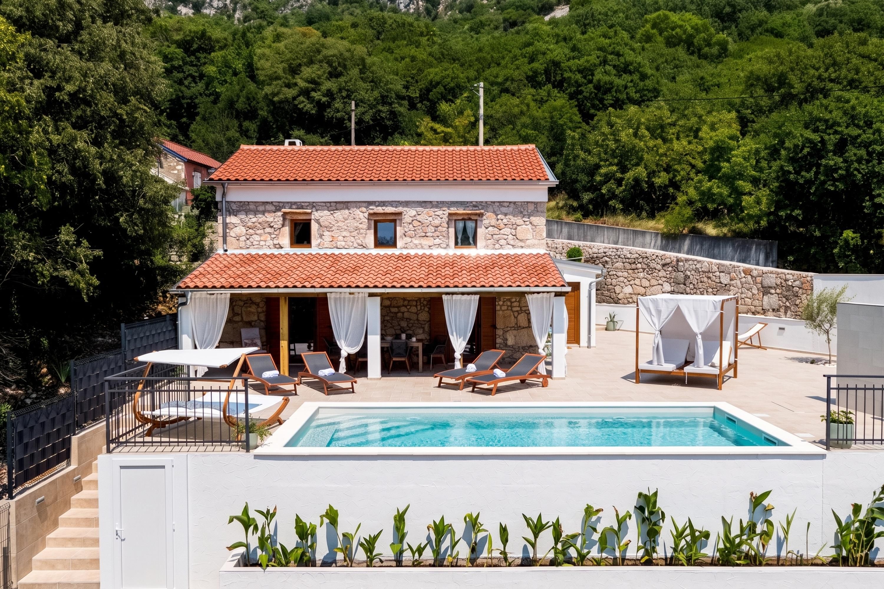 A two-story building with a swimming pool, outdoor seating, and a stone wall.