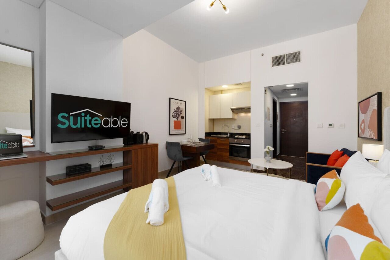 A hotel room with a bed, a desk, a television, and a kitchenette.