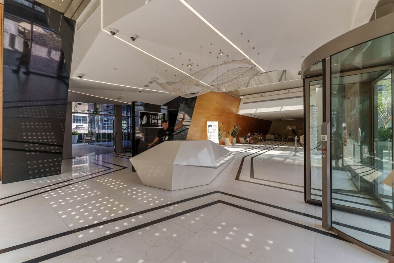 Un vestíbulo moderno con una estructura blanca central, paredes de vidrio y una escalera que conduce a los pisos superiores.