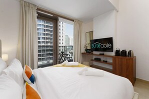 A hotel room with a large bed, a television, a wooden nightstand, and a view of the city through the window.