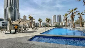 A rooftop pool area with a clear view of surrounding high-rise buildings, palm trees, and outdoor seating. - Your gateway in Sparkle Tower JBR by Suiteable (Dubai)