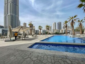 A rooftop pool area with a clear view of surrounding high-rise buildings, palm trees, and outdoor seating. - Your gateway in Sparkle Tower JBR by Suiteable (Dubai)