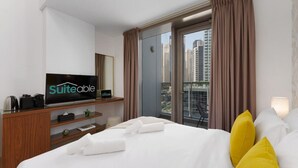 A hotel room with a bed, a television, a window with curtains, and a view of high-rise buildings. - Your gateway in Sparkle Tower JBR by Suiteable (Dubai)