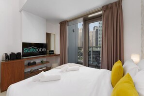 Habitación de hotel con cama, televisor, ventana con cortinas y vistas a edificios altos.