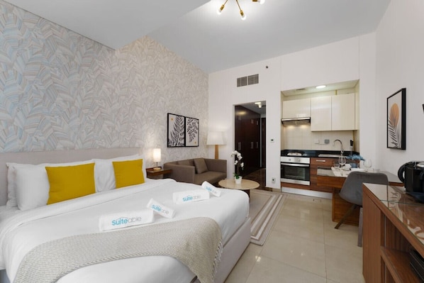 A modern hotel room with a bed, a sofa, a desk, and a kitchenette.