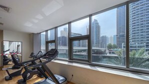 A gym with treadmills and exercise equipment, large windows with a city view. - Your gateway in Sparkle Tower JBR by Suiteable (Dubai)