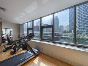 A gym with treadmills and exercise equipment, large windows with a city view. - Your gateway in Sparkle Tower JBR by Suiteable (Dubai)