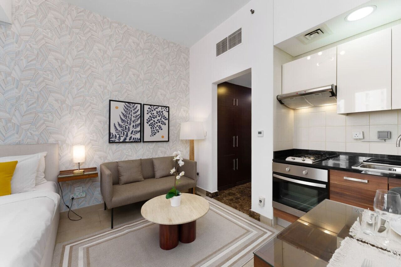 Una habitación de hotel moderna con sofá, una mesita redonda, cama y kitchenette.