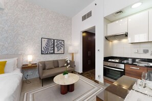Una habitación de hotel moderna con sofá, una mesita redonda, cama y kitchenette.
