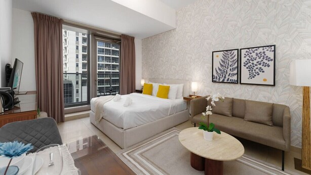 A hotel room with a bed, a sofa, a round coffee table, and a large window with curtains. - Your gateway in Sparkle Tower JBR by Suiteable (Dubai)