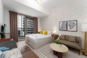 A hotel room with a bed, a sofa, a round coffee table, and a large window with curtains.