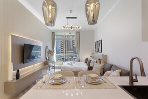A modern hotel room with a dining area, a TV mounted on the wall, a large window, and a sofa.