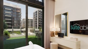 A hotel room with a large bed, a TV, a desk with a laptop, and a view of modern buildings. - Chic 1BR Apartment in Azizi Riviera, Meydan (Dubai)