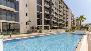 A modern building with a swimming pool, balconies, and a clear sky. - Chic 1BR Apartment in Azizi Riviera, Meydan (Dubai)