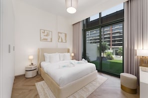 Una habitación de hotel moderna con una cama grande, una mesita de noche, un pequeño taburete y una ventana con vistas a un edificio.