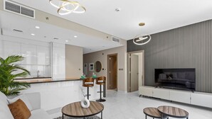 A modern living room with a sofa, two round tables, a TV, and a kitchen area.