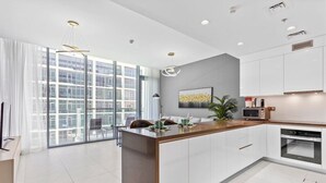 A modern kitchen with a central island, white cabinetry, and a large window offering a city view.