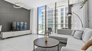 A modern living room with a sofa, a coffee table, a TV, and a large window with a view of buildings.