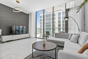A modern living room with a sofa, a coffee table, a TV, and a large window with a view of buildings.