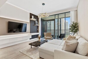 A modern living room with a sofa, a coffee table, a TV mounted on the wall, and a balcony with a view of the city.