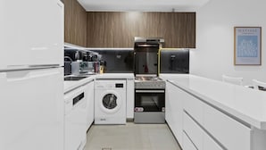 Une cuisine compacte équipée d’un lave-linge, d’un four encastré et d’une machine à café.