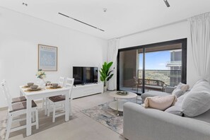 A modern living room with a dining area, a large window with a city view, a flat-screen TV, and a framed artwork on the wall. - Stunnigly furnished and spacious apartment in JVC (Dubai)