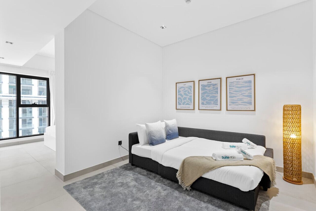 A modern bedroom with a bed, a grey rug, and a large window.