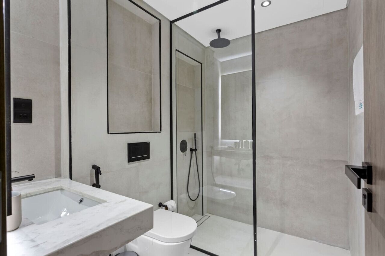 Et moderne badeværelse med bruseniche i glas, vask i marmor og toilet.