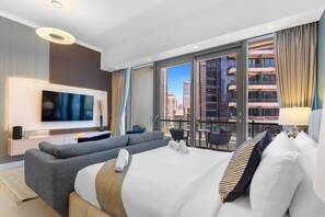 A modern hotel room with a large bed, a flat-screen TV, a sofa, and a balcony with a city view.