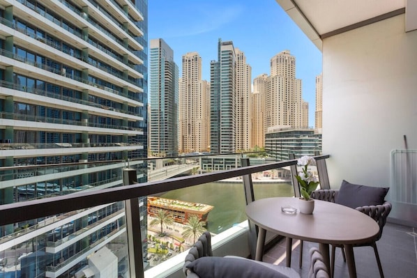 A balcony with a table and chairs, overlooking a cityscape with high-rise buildings and a river.