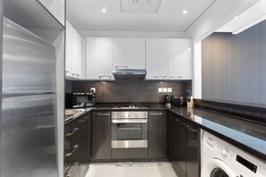 A modern kitchen with stainless steel appliances, dark cabinetry, and a built-in washing machine.
