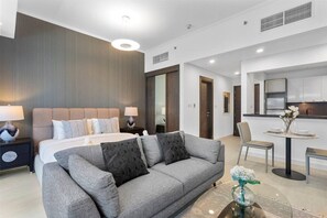 Una habitación de hotel moderna con cama, sofá gris, mesa de comedor con sillas y kitchenette.