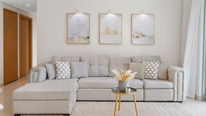 Ein modernes Wohnzimmer mit einem grauen Ecksofa, einem kleinen runden Tisch mit einer Vase und drei gerahmten abstrakten Gemälden an der Wand.