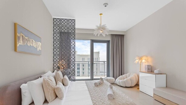 A modern bedroom with a large bed, a view of the city through a balcony, and a decorative wall panel.