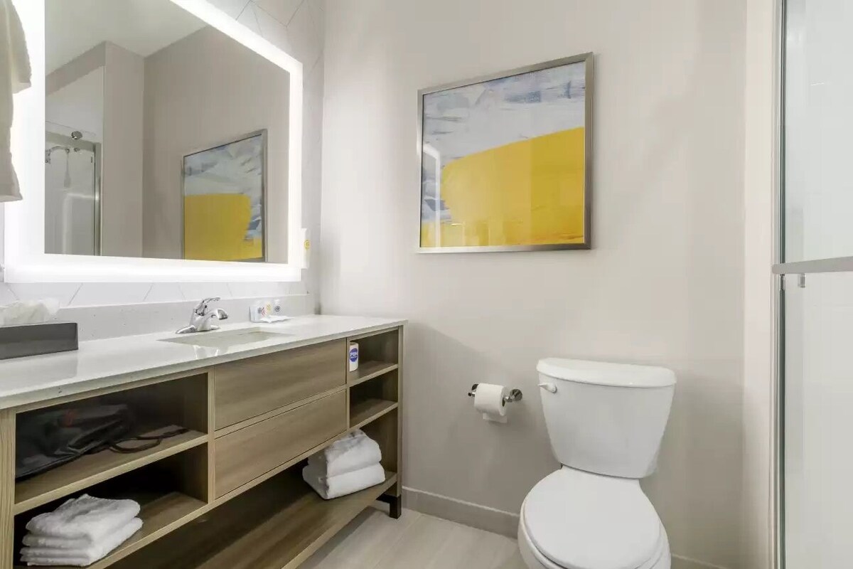 Uma casa de banho moderna com um espelho grande, uma pia, uma sanita e uma prateleira com toalhas.