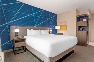 Habitación de hotel con una cama grande, dos mesitas de noche con lámparas, una pared con diseño geométrico, un cuadro y un armario empotrado.