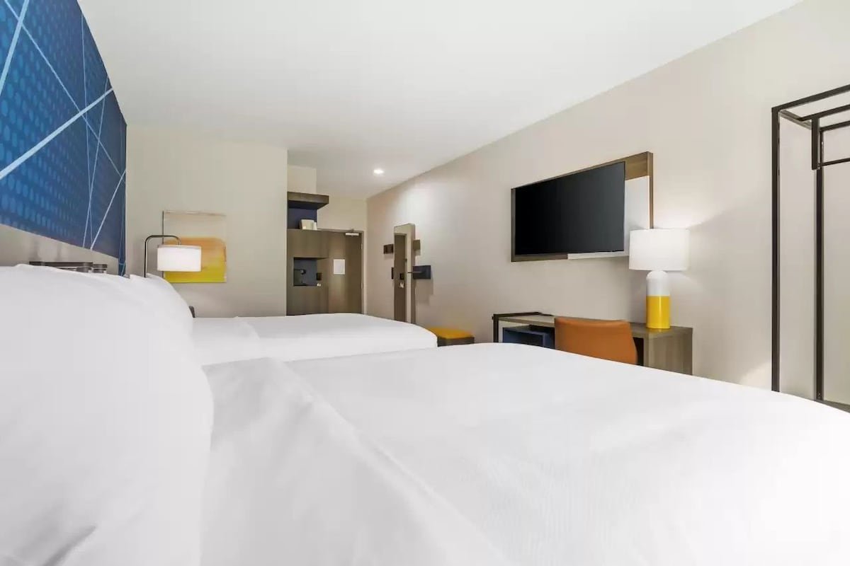 Quarto de hotel com duas camas, televisão, escrivaninha e banheiro.