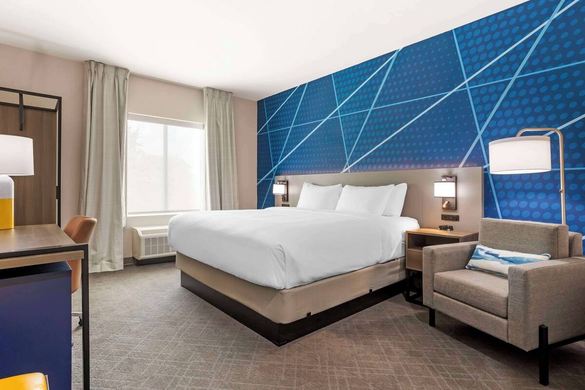 A hotel room with a large bed, a desk, a chair, and a blue patterned wall.